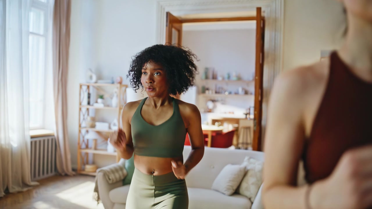 Primo piano di donne che fanno allenamento cardio a casa. Amiche multietniche si esercitano in soggiorno.