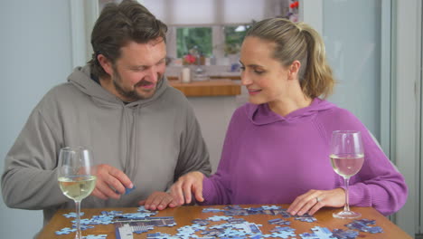 couple sitting at table at home with glass of wine doing jigsaw puzzle together