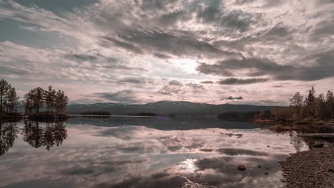 clouds, colored by the setting sun in the shades of pink, gray and yellow, reflected in the mirrorlike waters of the lake