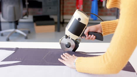 biracial female fashion designer using rotary fabric cutter in studio, slow motion