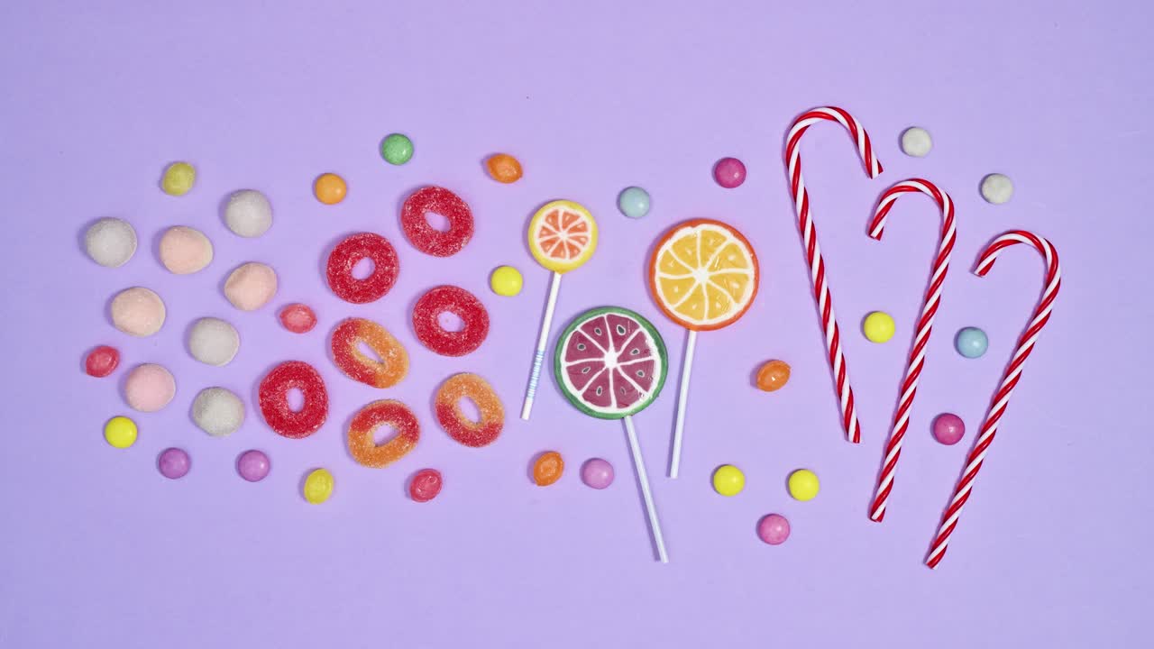 las piruletas, los caramelos de colores y los caramellos de goma aparecen sobre un fondo púrpura pastel.