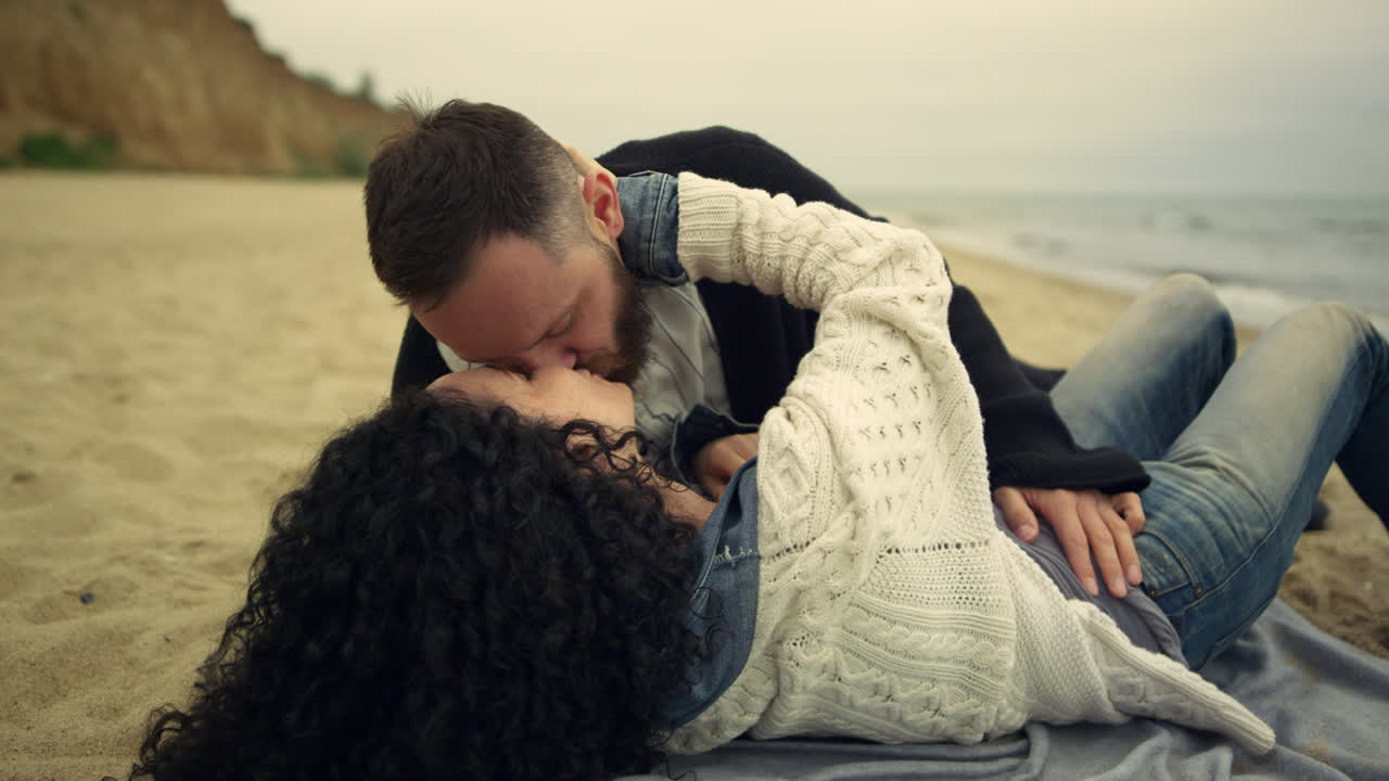 una pareja coqueteando besándose en la playa junto al mar, dos amantes tocándose en la naturaleza.
