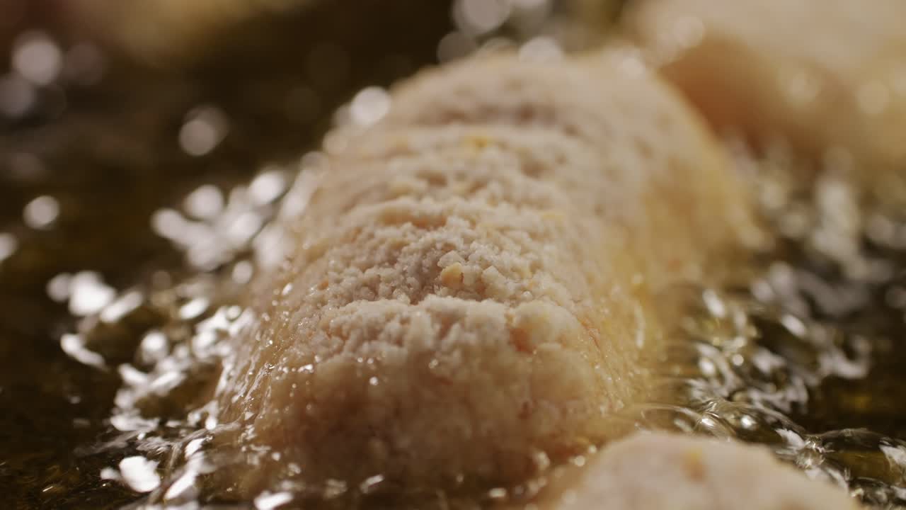 Portuguese croquettes broiling on black frying pan close-up macro. Breaded croquette of fish, potatoes and ham. Man cooking spanish food. High quality 4k footage