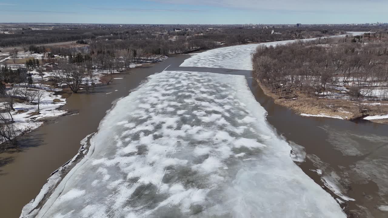 Lavtflyvende drone, der langsomt flyver langs Red River syd for Winnipeg, Manitoba, Canada. Forårsopbrud med delvist frossen overflade, drivende isflager, åbne vandkanaler.