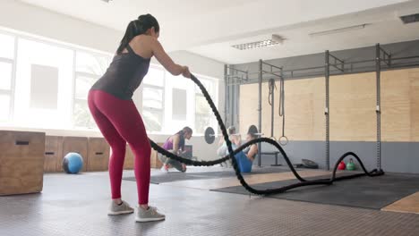 focused unaltered biracial woman exercising with battling ropes at gym, in slow motion