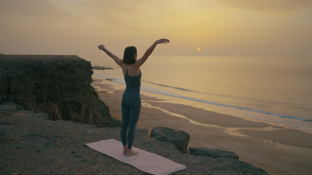 Woman practicing yoga at a breathtaking coastal sunset