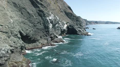 Cinematic-low-altitude-circular-move-around-a-huge-cliff-with-waves-crashing-on-the-big-rocks-revealing-the-long-Pacific-coastline-near-Ragged-Point-by-Highway-1-in-California,-USA