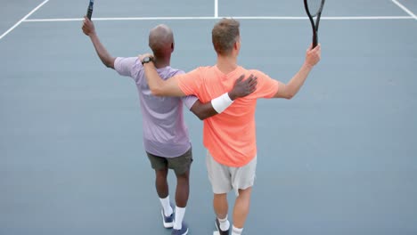 Rear-view-of-two-diverse-male-friends-playing-doubles-celebrating-win-on-court-in-slow-motion