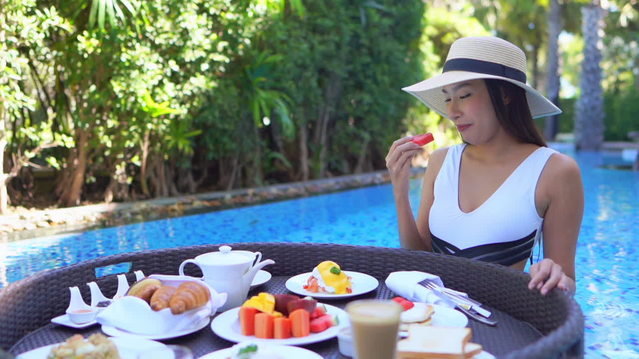 Asian young woman tourist has her own personal breakfast on a floating table in a private swimming pool