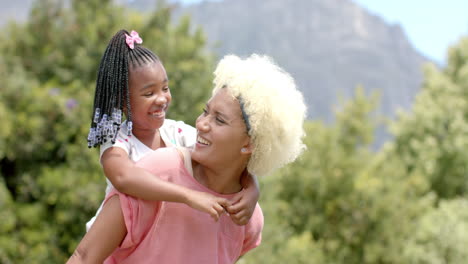 Una-Joven-Madre-Birracial-Con-Cabello-Rubio-Lleva-A-Una-Hija-Afroamericana-En-La-Espalda