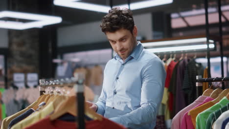 hombre cliente caminando filas de ropa en la boutique primer plano. cliente satisfecho sonriendo