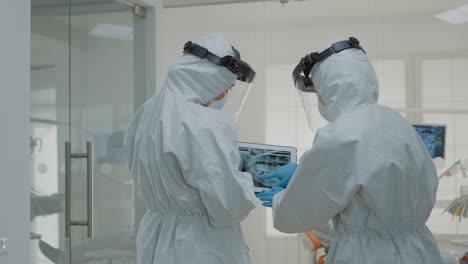 estomatólogos con trajes de ppe sosteniendo tableta digital con rayos x de los dientes