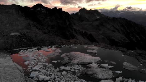 Spinning-aerial-view-above-a-glacier-lake-full-of-melted-icebergs-in-remote-parts-of-the-Swiss-Alps-with-sunset-glow-behind-mountain-peak