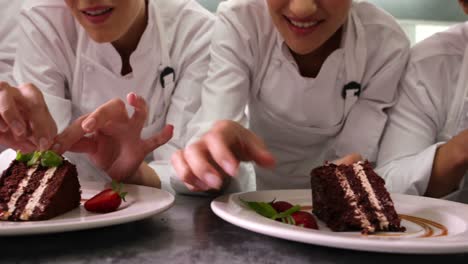 line of chefs garnishing dessert plates with mint leaves and strawberries