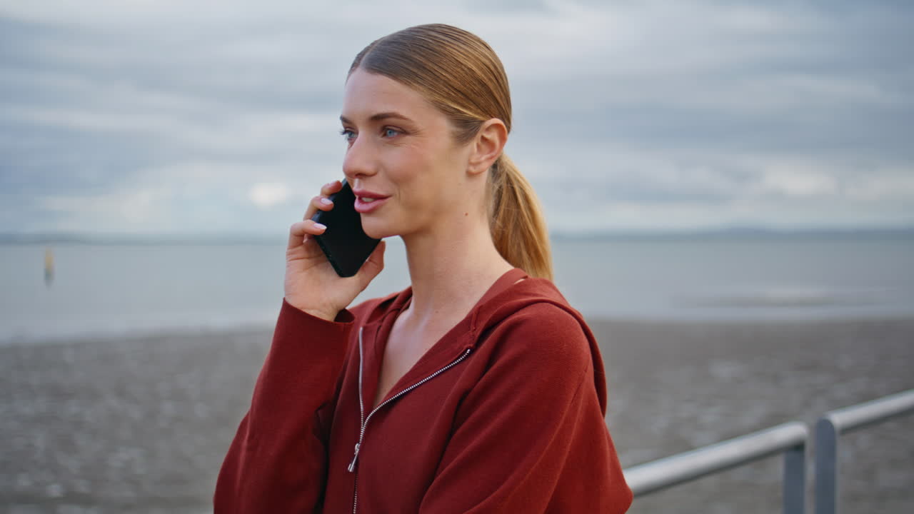 Girl having smartphone conversation at cloudy beach. Closeup casual woman talk