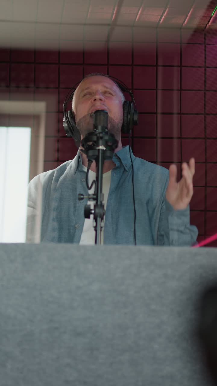 un hombre canta apasionadamente en un estudio de grabación, con auriculares negros y una camisa azul de manga larga. la escena captura su intensa expresión mientras canta con la boca abierta