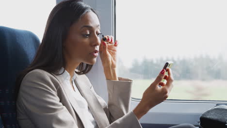 businesswoman sitting in train commuting to work putting on make up using mobile phone as mirror