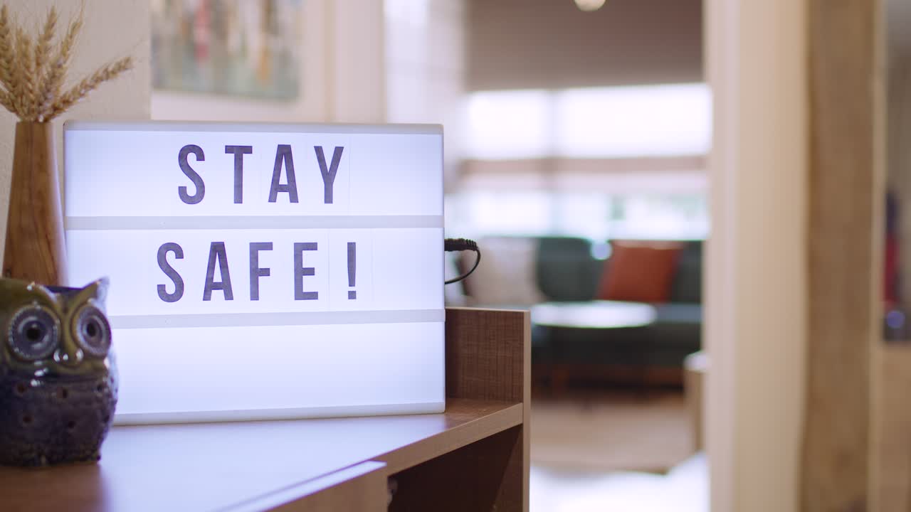 Woman walks in and Switches on Decorative Lightbox Written Stay Safe in Comfy and Cozy Home