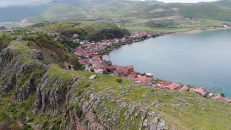 vista de avión no tripulado en albania volando sobre una pequeña ciudad con casas al lado de una colina verde en el lago ohrid con agua azul cristalino