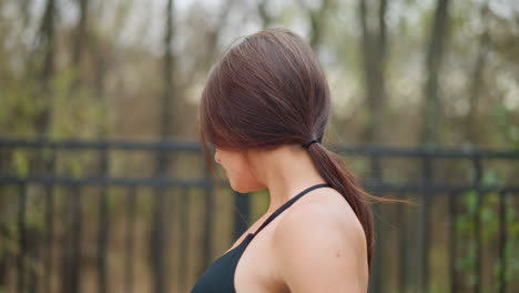 Closeup of woman stretching neck in neck top near iron fence with blurred trees in background, highlighting flexibility, relaxation, and wellness in a natural outdoor setting