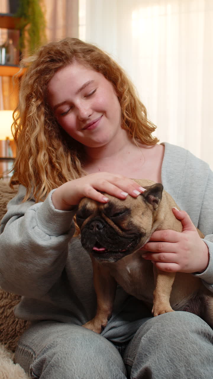 Young woman gently petting pug dog on home sofa with affection and calm expression in quiet moment