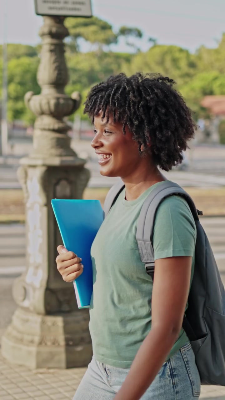 Studente afroamericano felice che cammina e usa il telefono per strada in città