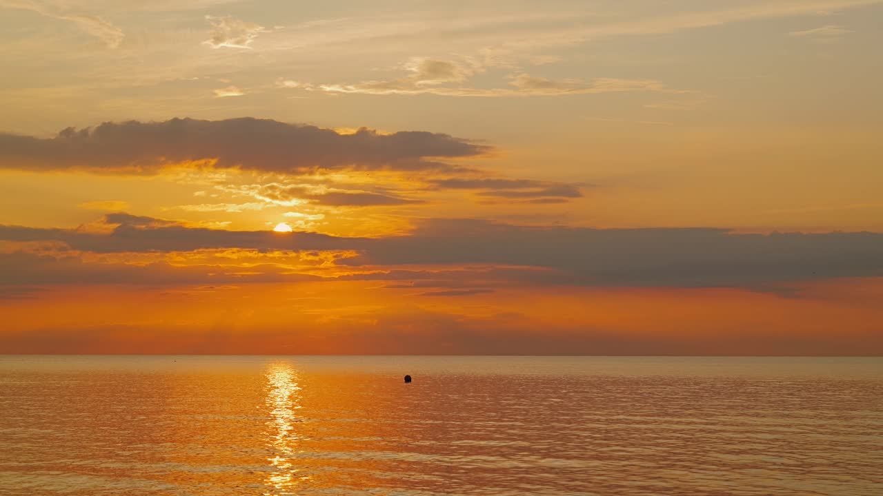 Handheld shot of vivid sunset sky with buoy on horizon reflecting golden light