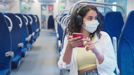 mujer usando teléfono en el tren con auriculares y máscara