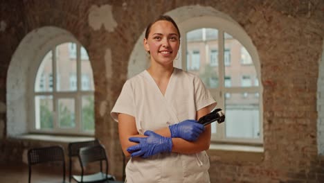 Retrato:-Una-Doctora-Profesional-Con-Un-Uniforme-Médico-Blanco-Se-Encuentra-Frente-A-Un-Fondo-De-Paredes-De-Ladrillo-Y-Grandes-Ventanas-Blancas.