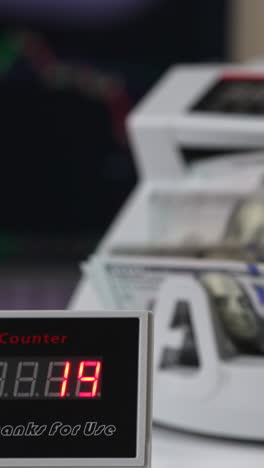 bill counter screen with red numbers growing quickly. hand puts us dollars into machine to count at backdrop in blur. vertical video