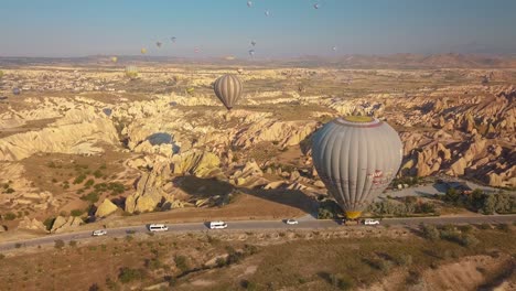 flying over mountains and fairy chimneys of goreme in red valley, hot air balloon being transported on road below