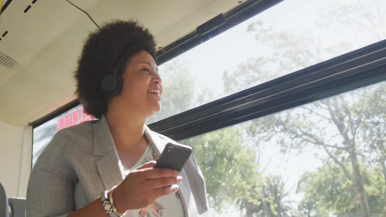 mujer biracial feliz de talla plus usando un teléfono inteligente en el autobús