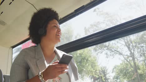happy plus size biracial woman using smartphone in bus