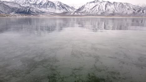 Low-angle-flyover-frozen-Crowley-lake-and-snowy-mountains-in-the-southern-Mono-County,-California,-United-States