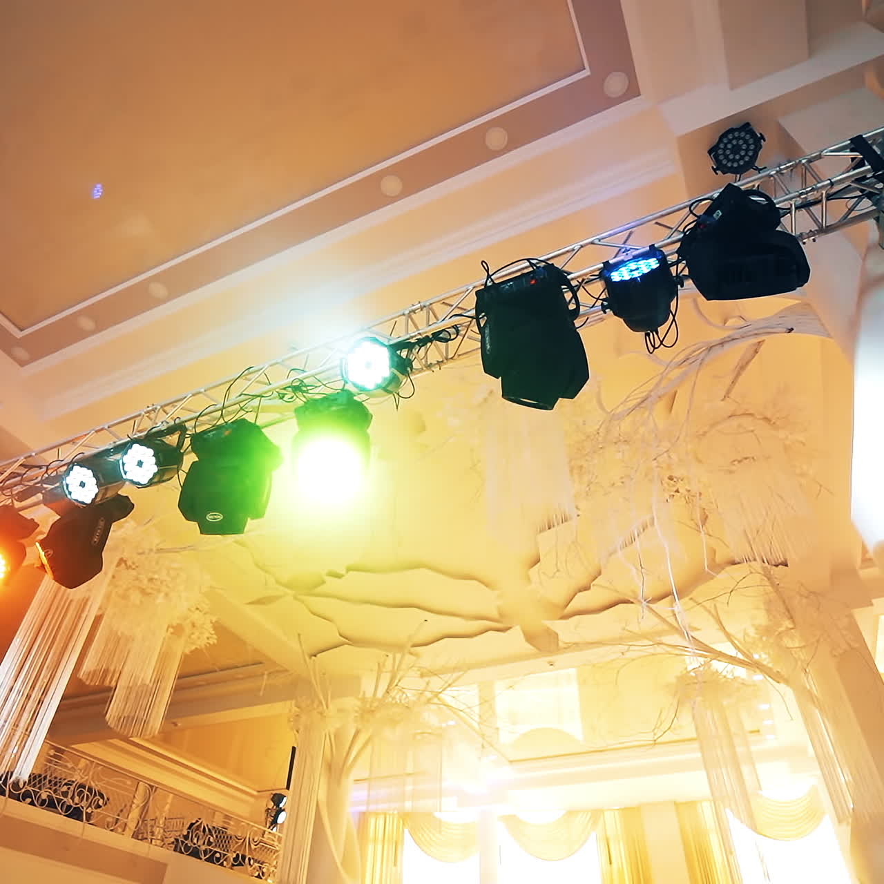 Black projectors hanging from top in the light concert hall. Metal construction with colorful spotlights on the creamy background indoors.