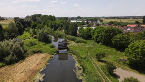 Flyover-above-tree-lined-stream-running-through-Batya,-Hungary