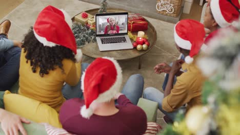 Eine-Vielfältige-Familie-Mit-Weihnachtsmützen-Nutzt-Laptop-Für-Einen-Weihnachtsvideoanruf-Mit-Einer-Glücklichen-Frau-Auf-Dem-Bildschirm