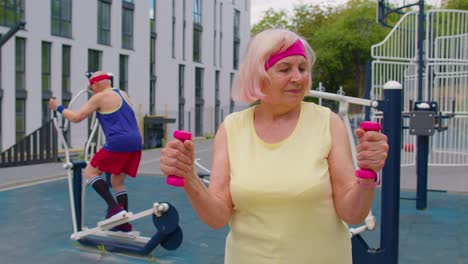 Senior-woman-grandmother-doing-active-training-weightlifting-exercising-with-dumbbell-on-playground