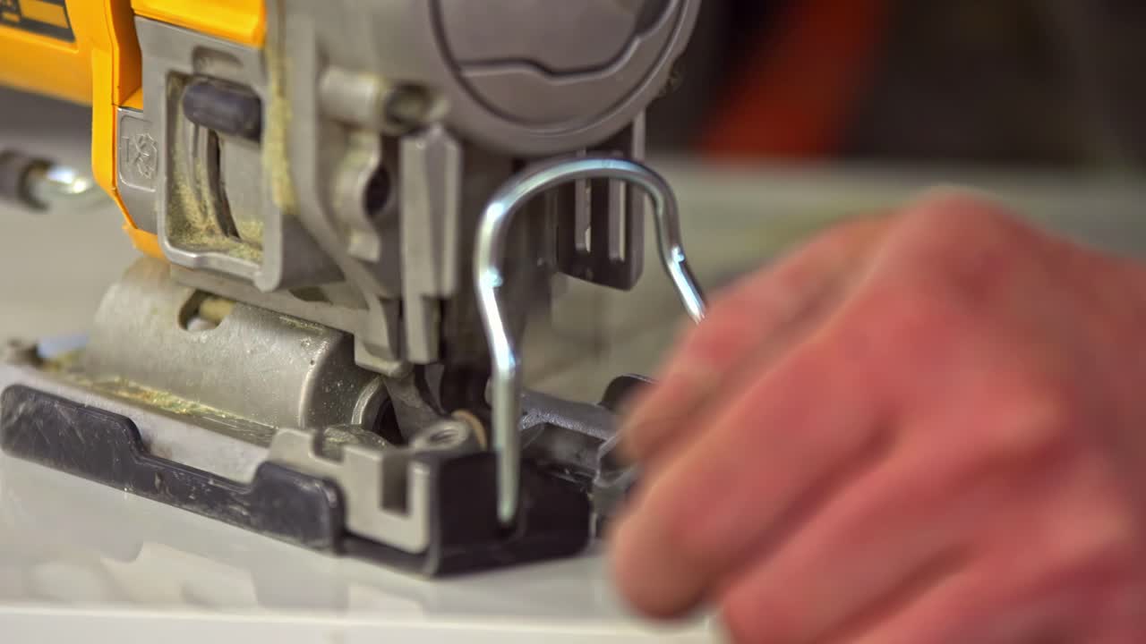 A detailed close-up shot shows a carpenter using a jigsaw to precisely cut a sheet of fiberboard during the manufacturing or assembly of kitchen furniture in a factory