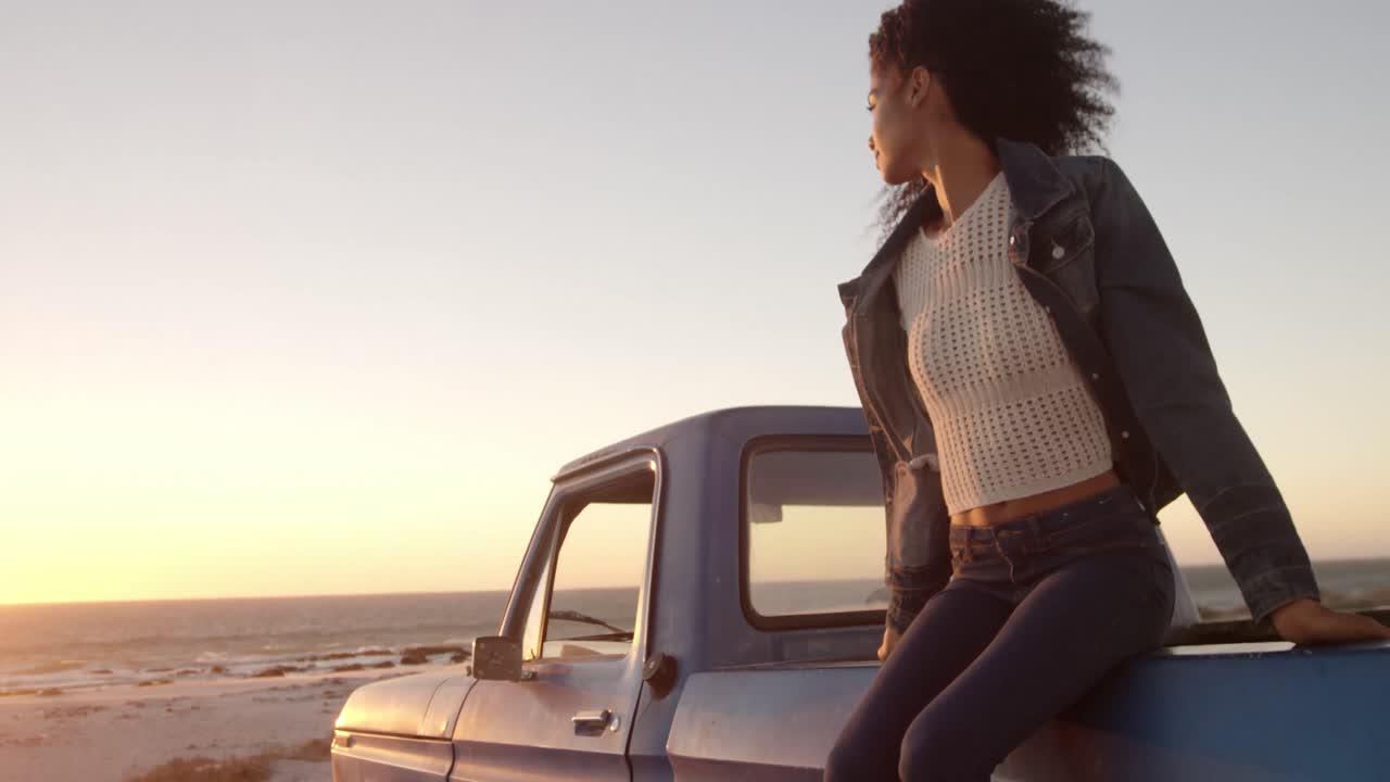Donna seduta sul cassone di un pickup in spiaggia 4k