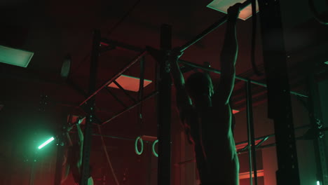 adult athletes are training in gym in darkness man and woman are jumping and doing pull-ups