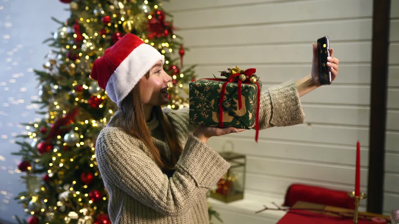 mujer tomando una selfie con un regalo de navidad cerca de un árbol de navidad
