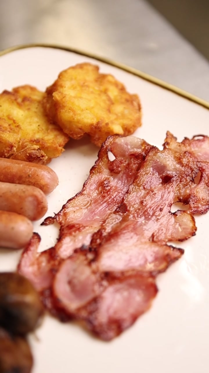 Primo piano di un abbondante piatto per la colazione con pancetta, salsicce e hash brown