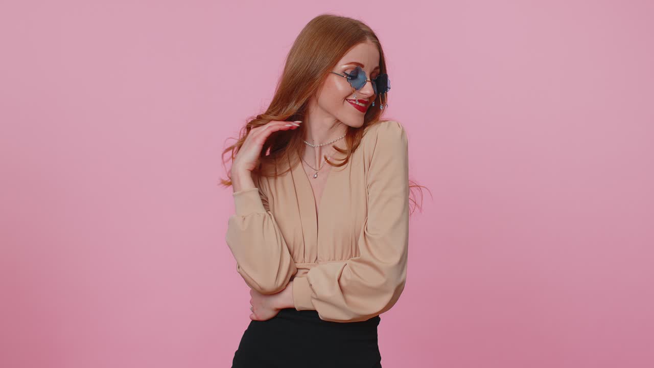 Sincere cool cheerful brunette girl in beige blouse wearing sunglasses charming smile on pink wall
