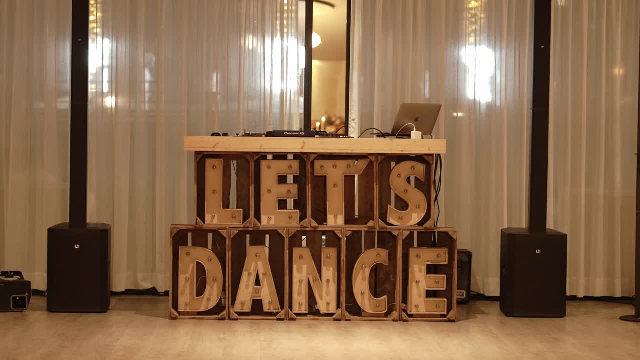 DJ booth with glowing "Let's Dance" wooden letters in a stylish event venue