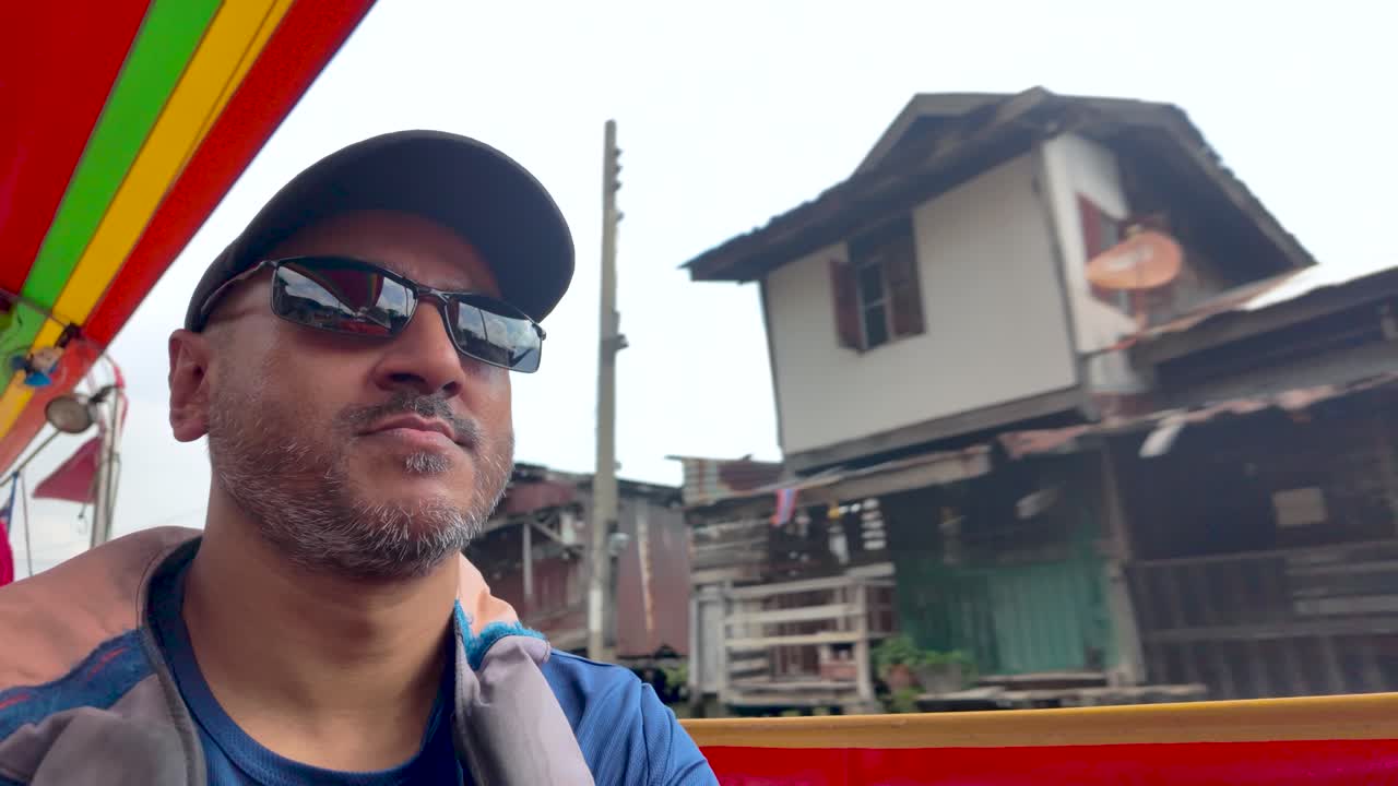 Male traveler wearing cap and sunglasses enjoys a river ride along Bangkok's Chao Phraya