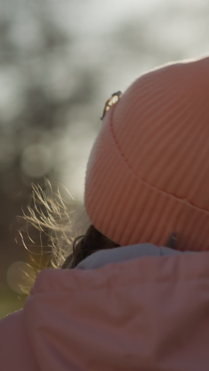 A little girl in a pink cap and jacket, joyfully holding a man's hand while walking outdoors. The girl looks up with a smile, and the warm sunlight creates a happy and serene atmosphere