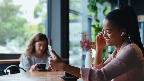 Joven-Empresaria-Con-Auriculares-Inalámbricos-Haciendo-Videollamadas-Por-Teléfono-Móvil-En-Una-Cafetería