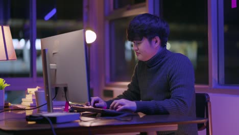 성인 아시아 남성 프리랜서 스웨터를 입고 늦은 밤 집에서 일하는 아시아 남성 젊은 성인 집에서 공부하는 방에서 혼자 옷 옷 셔츠를 입고 데스크 pc 앞에서 일합니다.
