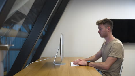 joven de perfil, código de vestimenta informal, trabajando en pc en una oficina moderna